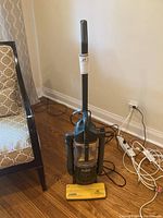 Full view of upright Eureka vacuum cleaner showing handle, hose, power cord, and yellow base.