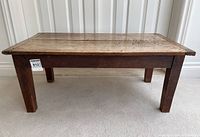 Front view of the antique wooden coffee table showing its rectangular shape, four square legs, and worn wood surface.
