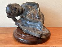 Side view of dark grey soapstone sleeping figure sculpture on wooden base, showing sculpted features like face, arm, legs, and chest.