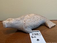 Side view of the entire fossilized whalebone seal sculpture showing shape and size relation to auction tag.