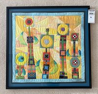 Full view of framed quilt showing abstract geometric design, blue mat and black frame