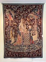 Full view of wool needlepoint tapestry depicting two women playing musical instruments under a floral and heraldic vine background