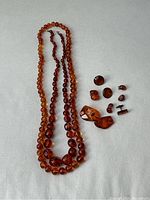 Two amber bead necklaces alongside assorted amber accessories displayed on a light surface.