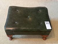 Top-down view showing rectangular shape, green vinyl upholstery with button tufts, slightly worn surface, carved wooden legs visible