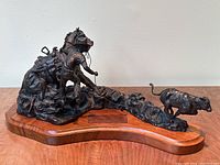 Full front view of bronze sculpture on wooden base showing cowboy, horse and cow