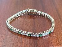 Bracelet laid flat showing alternating green and clear stones in bezel settings