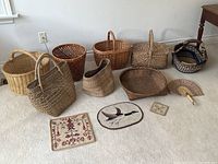 Overview image showing all eight woven baskets and three needlepoint textile pieces laid on a carpeted floor against a white wall.