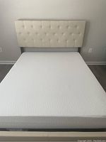 Beige colored platform bed with tufted headboard and white mattress, likely queen size
