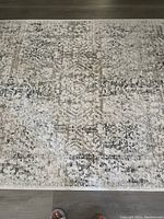 Top view of the area rug showing the overall abstract pattern and colors grey, tan, and white on hardwood flooring.