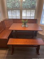 Full breakfast nook set in front of window with blinds, includes L-shaped bench, table, and separate bench in matching brown wood.