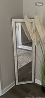 Floor mirror placed standing in a corner against a beige wall next to pampas grass decor.