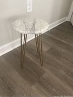 Side angled view showing round gray and white marble top and bronze hairpin legs on hardwood floor.
