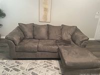 Charcoal grey sofa with chaise lounge, plush cushions and broad armrests set against a light wall, sitting on a patterned rug.