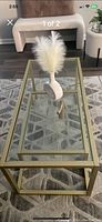 Top angled view of the rectangular bronze metal framed coffee table with glass surfaces and decorative white feather vase on top.