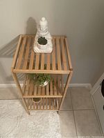 Wooden stand showing all three shelves with decorative plants and a Buddha statue on top, photo taken from front right angle.