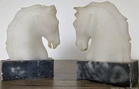 Front view of the pair of alabaster horse head bookends on marble bases, showing the carved details and overall condition.
