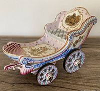 Side angle of the porcelain carriage showing detailed floral and figure painted motifs and four decorated wheels.
