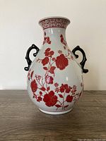 Front view of white Chinese porcelain vase decorated with red carnation flowers and two black scroll handles.