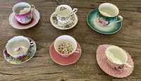 Six fine porcelain cups and saucers arranged on wood surface, showing variety of floral designs and colors.