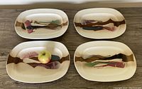 Four rectangular raku pottery stoneware serving dishes arranged with an apple on one dish showing scale and design colors.