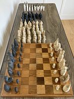 Two full sets of chess pieces arranged on wooden chess boards; one set is the cream and dark colored Lewis Chessmen pieces, the other is black and white onyx pieces with some red paint on the tops of a few pieces.