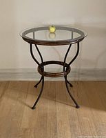 Full view of the round table showing glass top, rattan frame, and iron legs on hardwood floor.