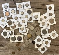 Top view of over 80 old coins, many sleeved with handwritten dates, scattered on wooden floor.