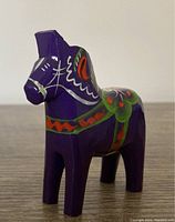 Front view of purple handpainted Dala horse wooden figurine with green, red, and white details.