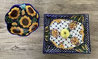 Two large Talavera Mexican pottery serving dishes placed on a wooden surface. One round dish with sunflower motifs and one rectangular dish with a lattice and floral pattern.