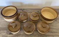 Front angle photo of 9 pieces in the lot featuring 4 large round baking bowls and 5 smaller round baking dishes with lids, showing the ribbed side design and two-tone brown and cream coloring.
