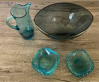 Photo showing vintage blue glass pitcher, centerpiece bowl, and a pair of bubble glass dishes on a wooden surface.