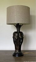 Full front view of lamp showing cast bronze base with three elephant heads and beige drum shade