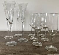 Photo showing 4 tall etched crystal champagne glasses and 6 tall clear crystal champagne flutes, arranged in rows on a wooden surface.