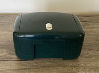 Closed dark green jewelry case with gold latch on a wooden surface.