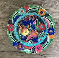 Top view of the brightly colored folk art painted plate with a small apple for size reference.