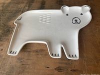 Top view of white bear-shaped ceramic plate with black outlines of face and paws on a wooden surface.