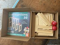 Open box showing the instruction guide book and wooden planks with balls inside the box.