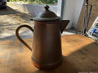 Side view of copper coffee kettle pot on wooden table with visible handle, spout, and lid, showing the condition and shape of the item.