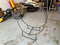 Wrought iron circular firewood holder on floor, showing circular frame and supporting legs, no firewood inside.