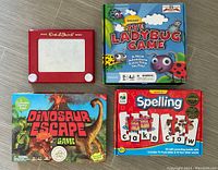 Photo showing all four items: red Etch A Sketch, Dinosaur Escape game box, The Ladybug Game box, and Spelling Puzzles box with wooden letters.