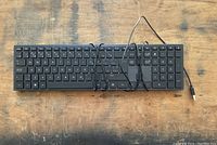 Photo of a black wired keyboard with USB cable on wooden surface showing all keys and numeric keypad.