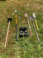 Overview of the landscaping tools laid on grass, showing various hand tools including hoes, shovels, and metal footings.