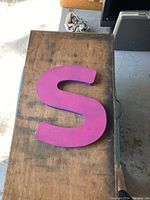 Large pink letter 'S' on wooden surface showing overall shape and color.