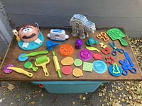 Full overview of all items laid out on table showing Play-Doh molds and tools including the dentist teeth head, pizza maker, cutters and various tools.
