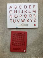 Photo of two Kid O magnet boards on the floor: one white alphabet letter board and one red magnetic drawing board with stylus.