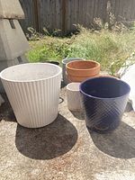 Top down photo of all plant pots showing variety of colors, shapes, and sizes situated on concrete outdoor surface in sunlight