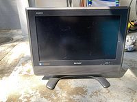 Front view of Sharp AQUOS monitor on feet with screen and branding visible.