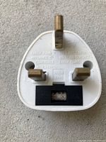 Front side of the white UK travel adaptor showing three brass prongs and fuse compartment