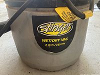 Close-up of the grey cylindrical tank with Stinger brand label showing wet/dry vacuum capacity of 2.0 gallons / 7.5 litre.