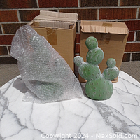 Two green ceramic cactus decorations, one wrapped in bubble wrap and the other unwrapped, both placed on a marble-like round table.